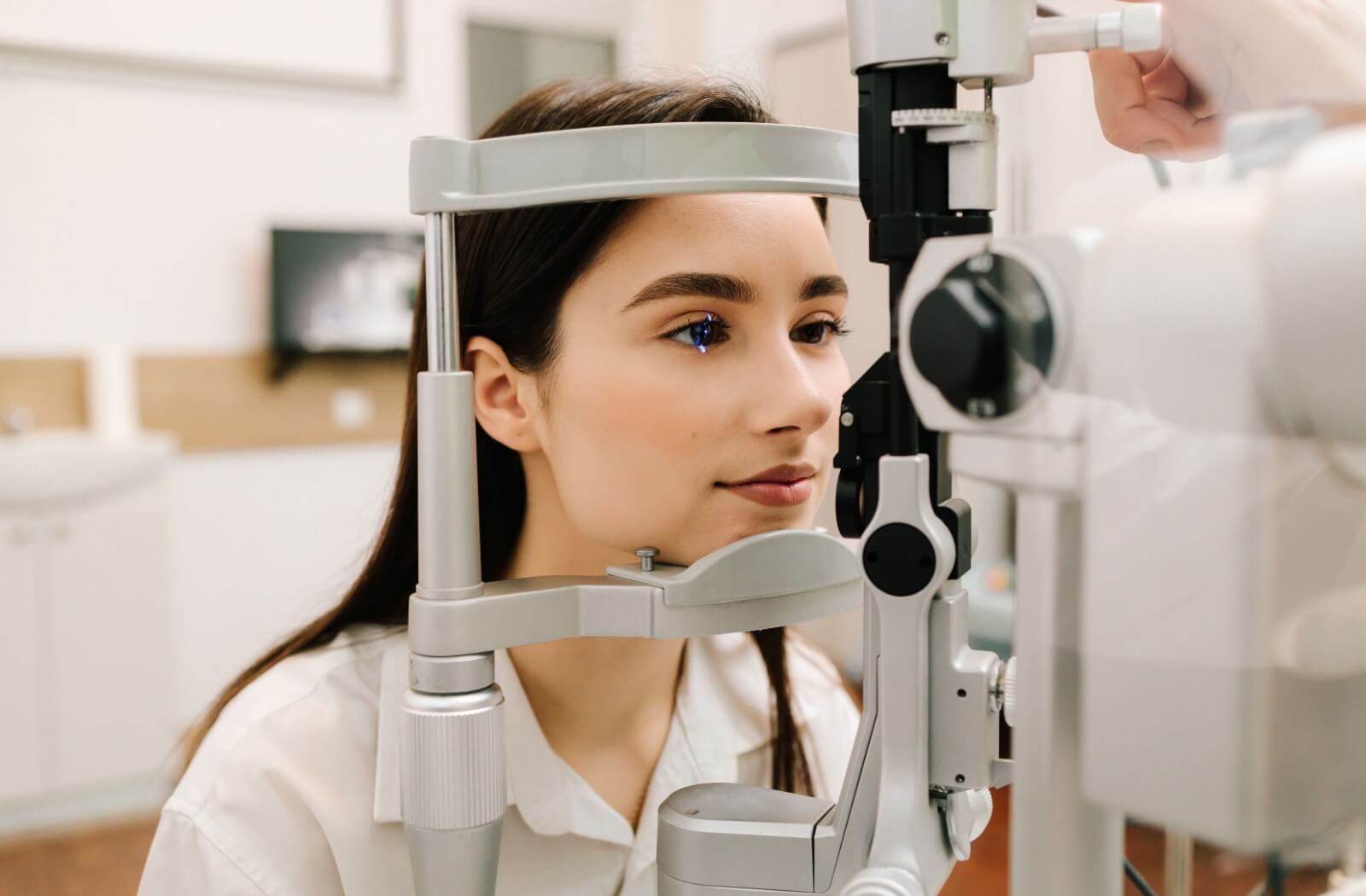 Woman sitting at a slit lamp while an optometrist performs an eye exam, with a blue light reflecting on her eye.