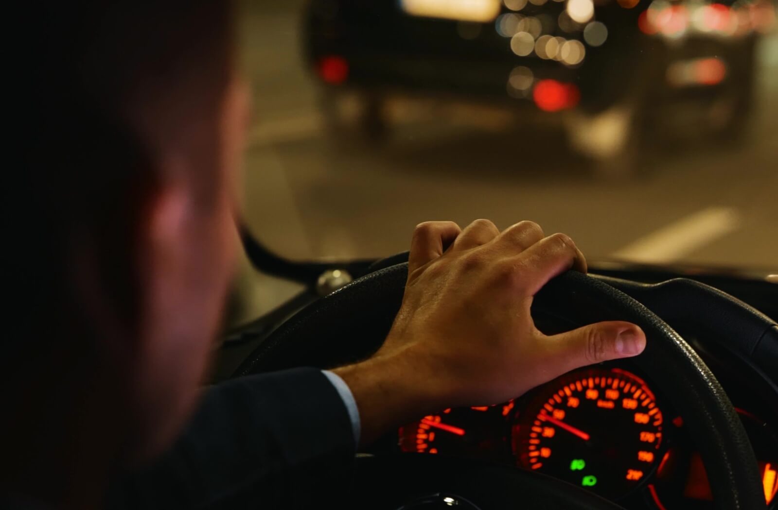 A person driving at night with hands on the steering wheel