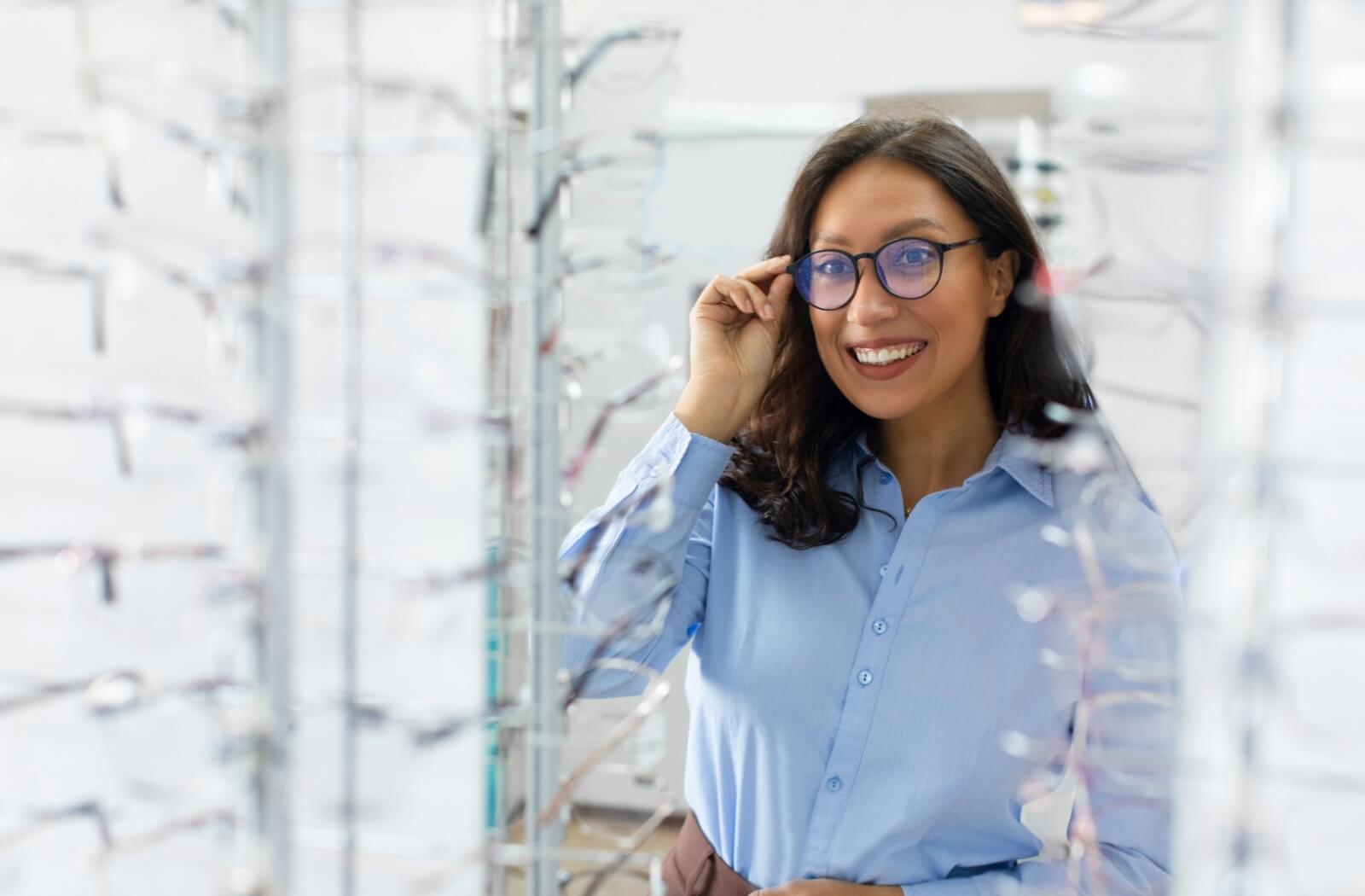 A smiling person trying on glasses in an optical shop, illustrating the benefits of progressive eyeglasses for seamless vision correction at all distances.