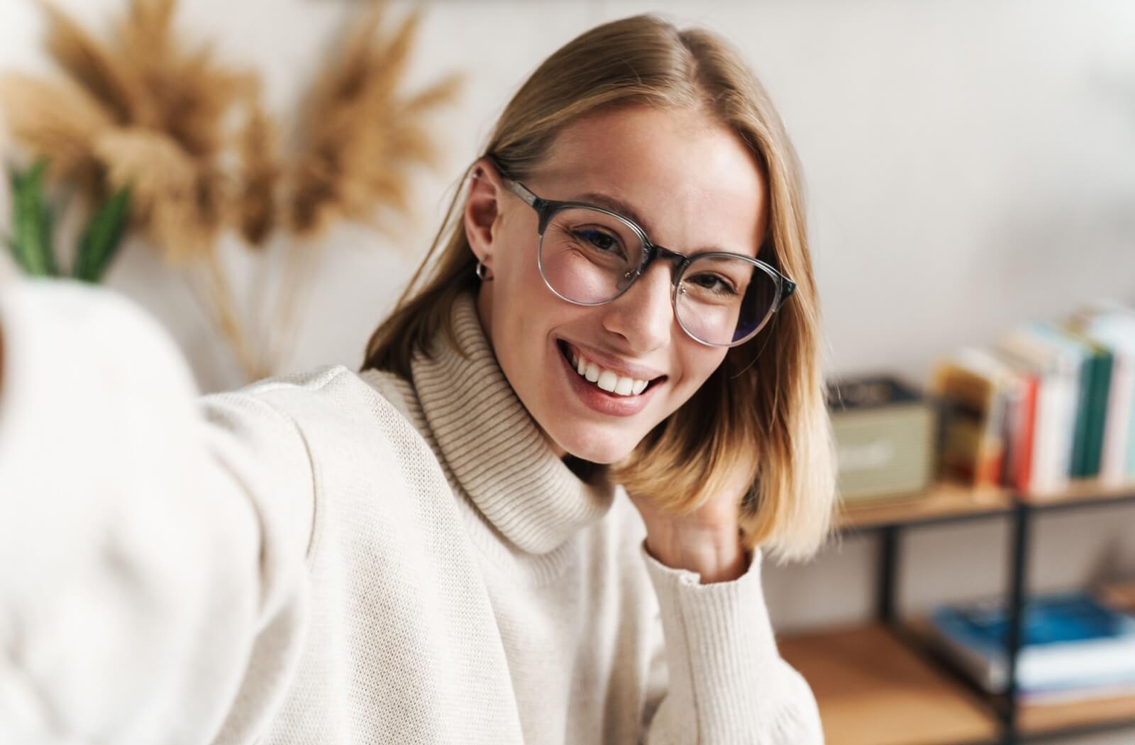 A smiling adult wearing stylish, round-rimmed eyeglasses and a turtleneck sweater.