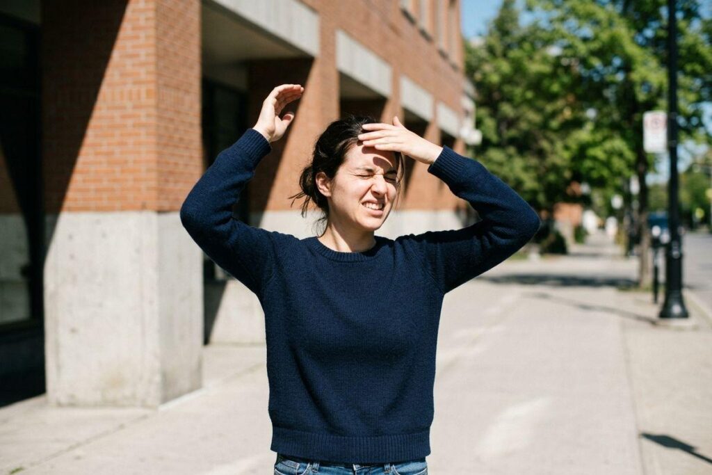 Person squinting and shielding their eyes from bright sunshine and UV glare outdoors.